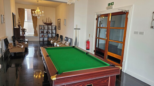 A billiards room with a pool table, chairs, a bookshelf, and a fire extinguisher. - The Strand Hotel (Eastbourne)