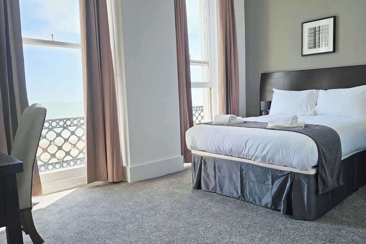 A hotel room with a bed, a desk, and a view of the sea.