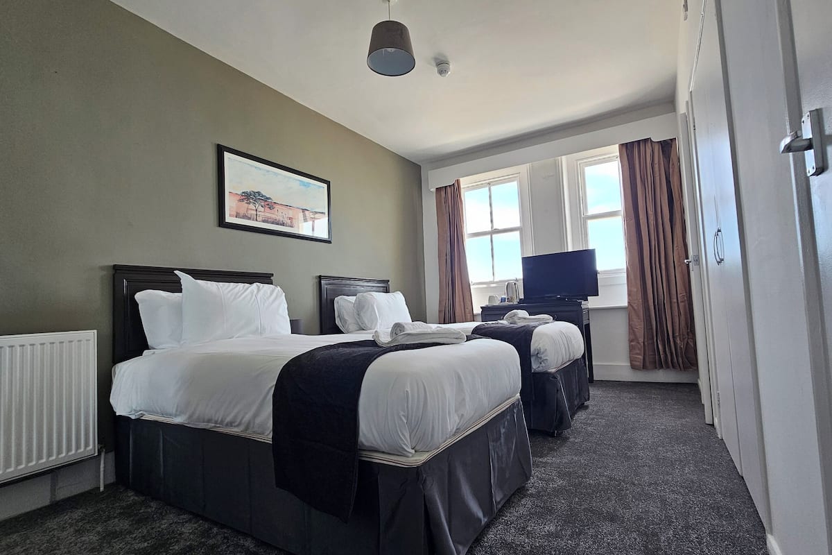 A hotel room with two beds, a television, a radiator, and a window with curtains.