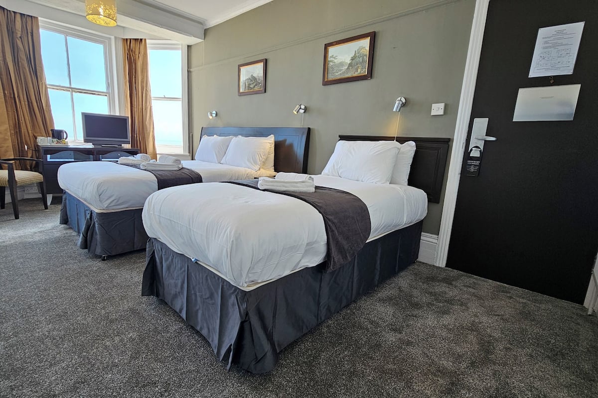 A hotel room with two beds, a desk, a chair, and a television.