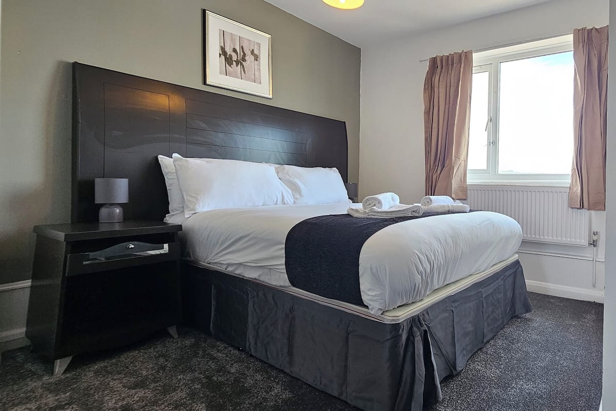 A neatly made bed with white linens, a dark headboard, and a small bedside table with a lamp.