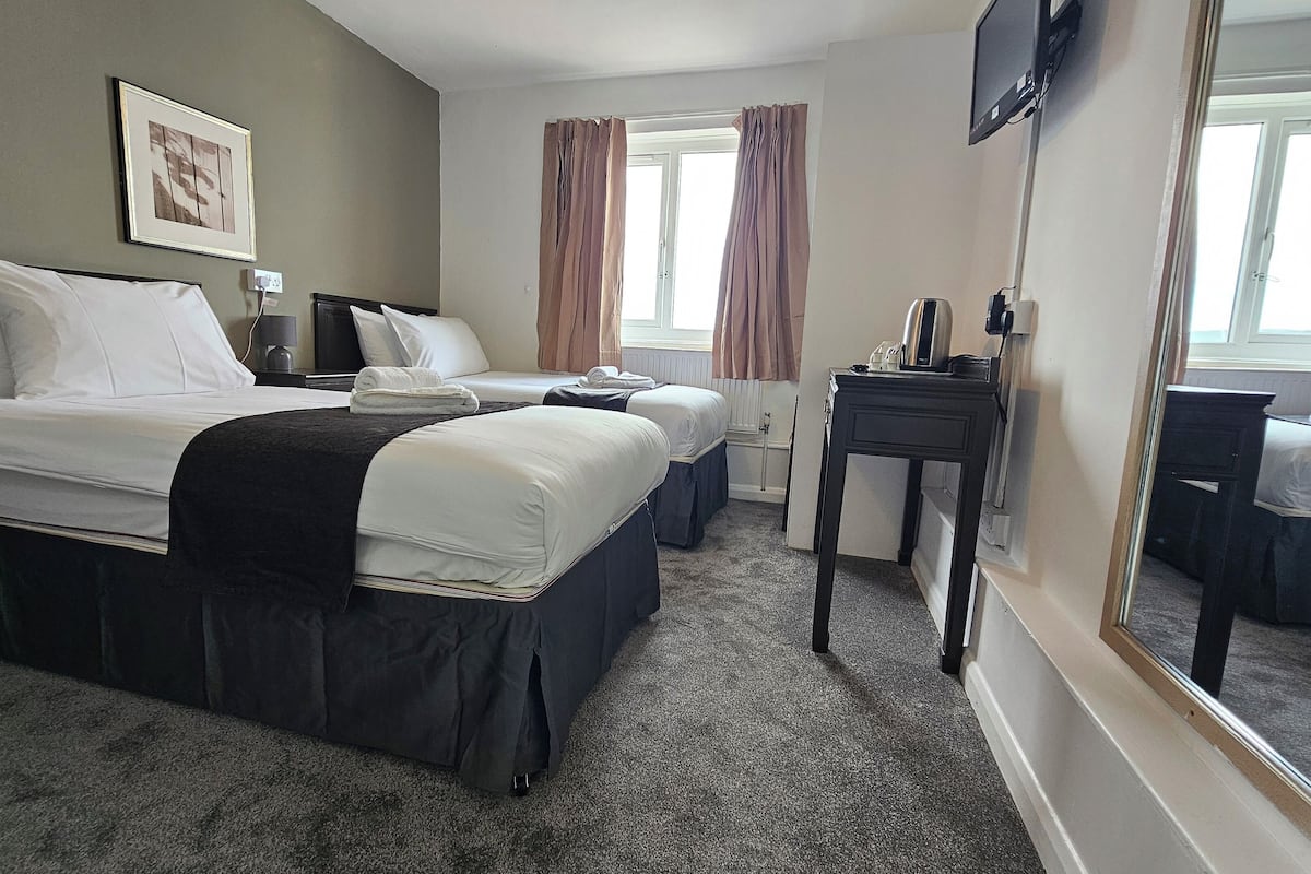 A hotel room with a large bed, two smaller beds, a desk, a mirror, and a TV.