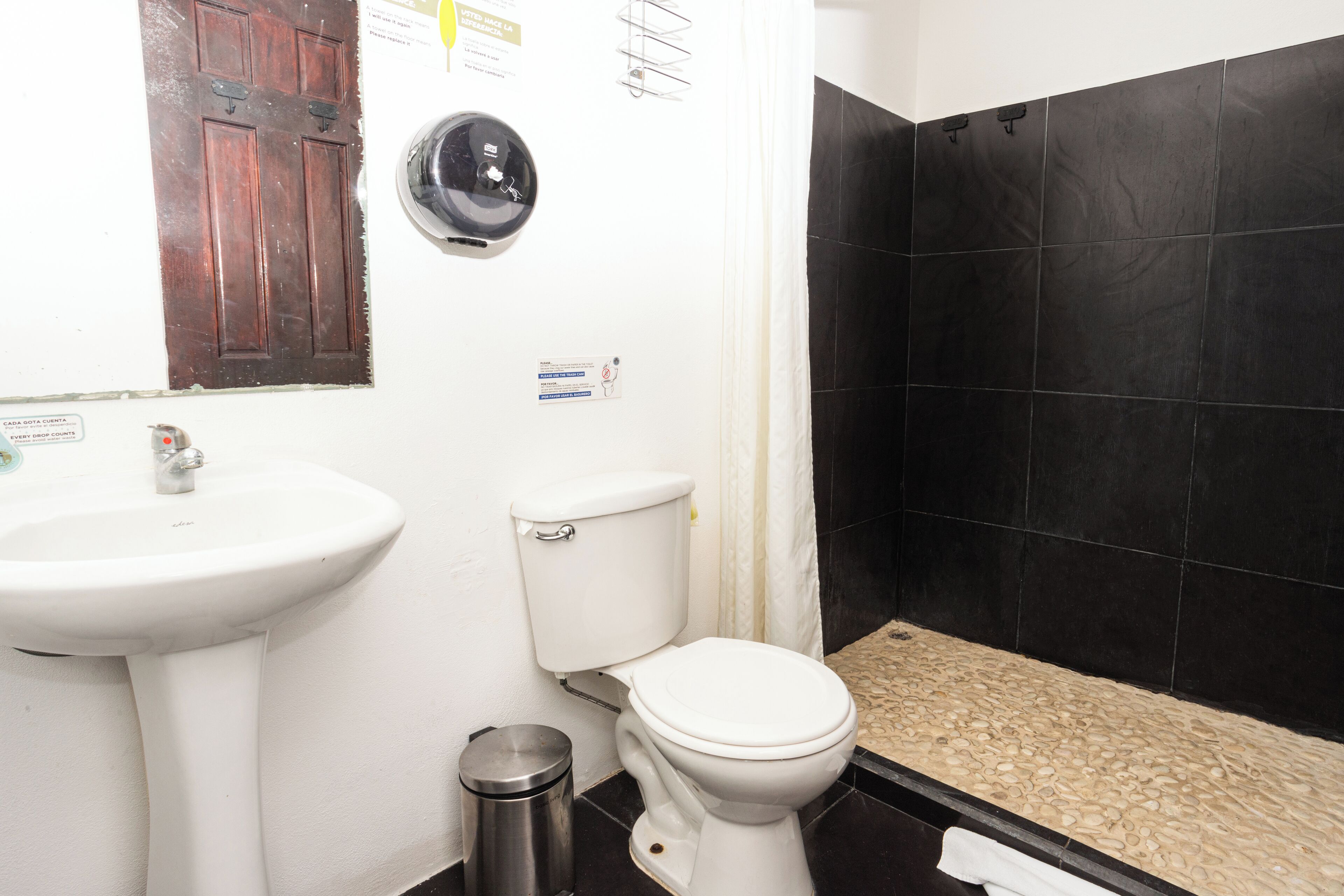 Un baño con lavamanos blanco, inodoro y zona de ducha con azulejos negros.