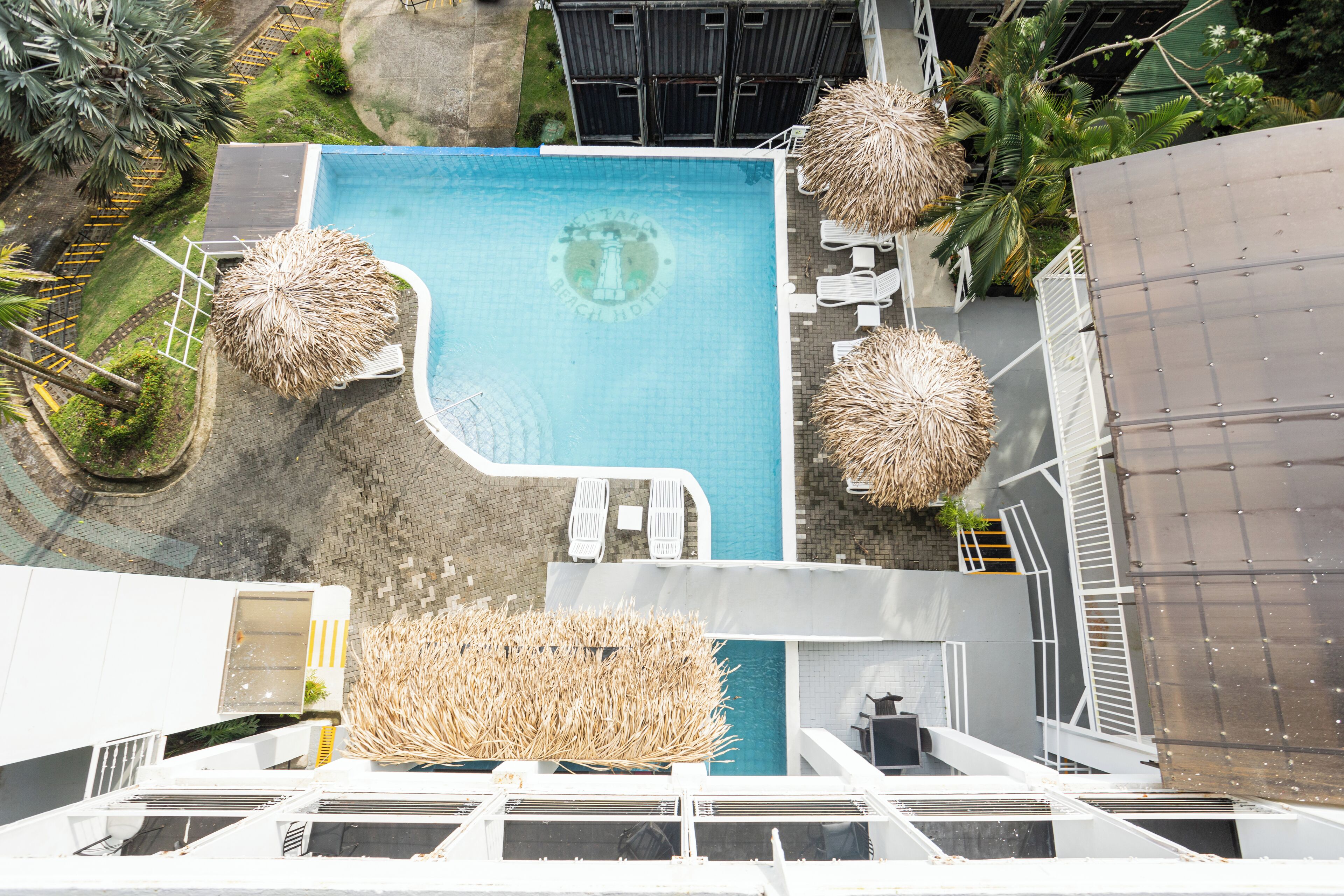 An aerial view of a rooftop pool with lounge chairs, thatched umbrellas, and a clear blue pool.