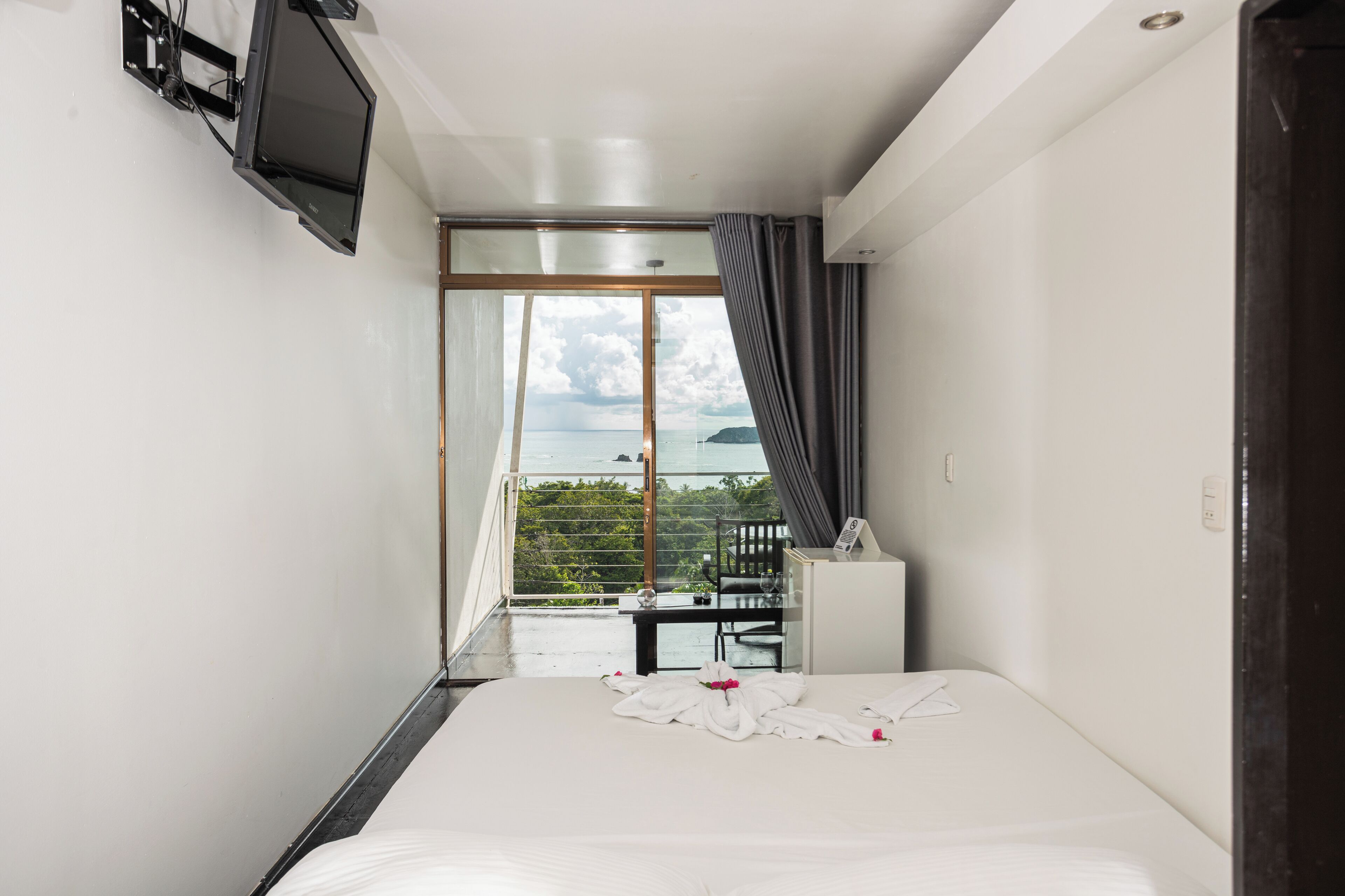 Quarto de hotel com uma cama, uma escrivaninha e uma TV fixada na parede.