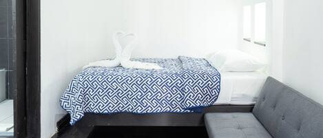 A small, clean room with a bed, a gray sofa, and a wall-mounted air conditioner.