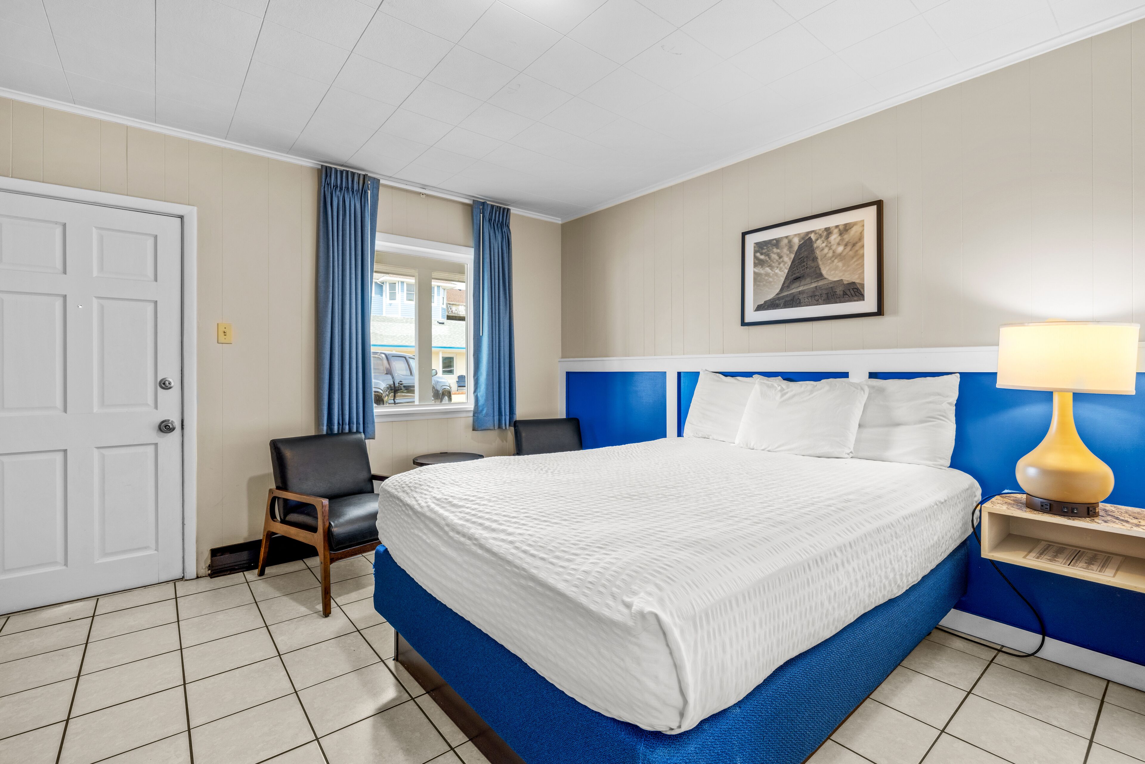 A hotel room with a large bed, a chair, a desk, and a window with curtains.