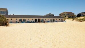 Un edificio frente a la playa con varias habitaciones, una playa de arena y cielo despejado.