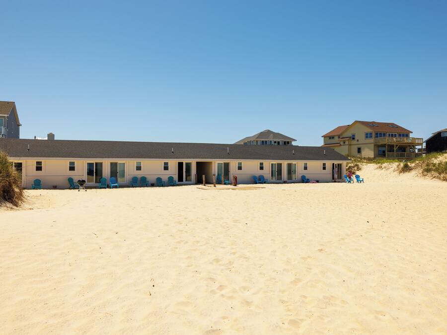 Un edificio frente a la playa con varias habitaciones, una playa de arena y cielo despejado.