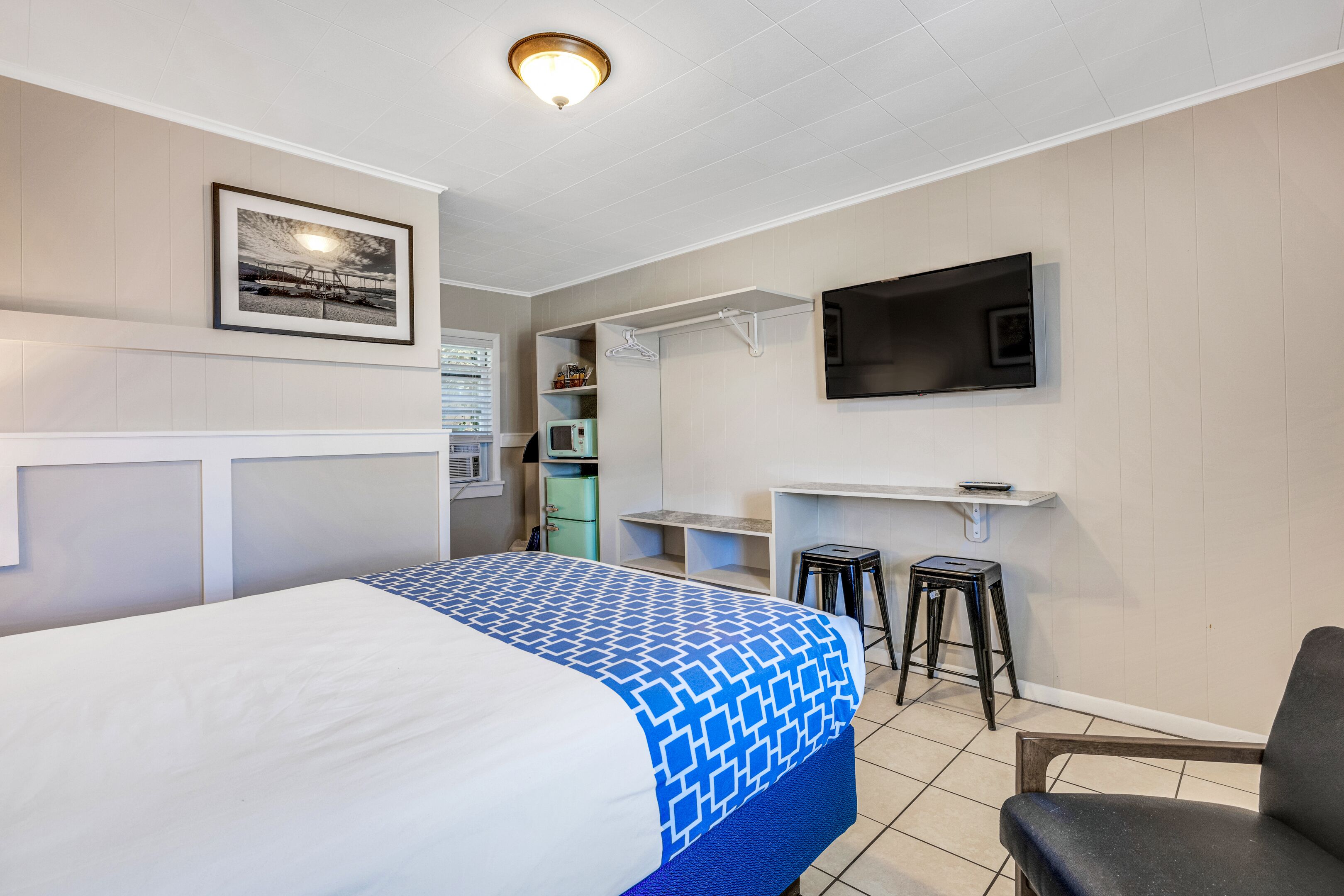 A hotel room with a bed, a desk, a TV, and a kitchenette.