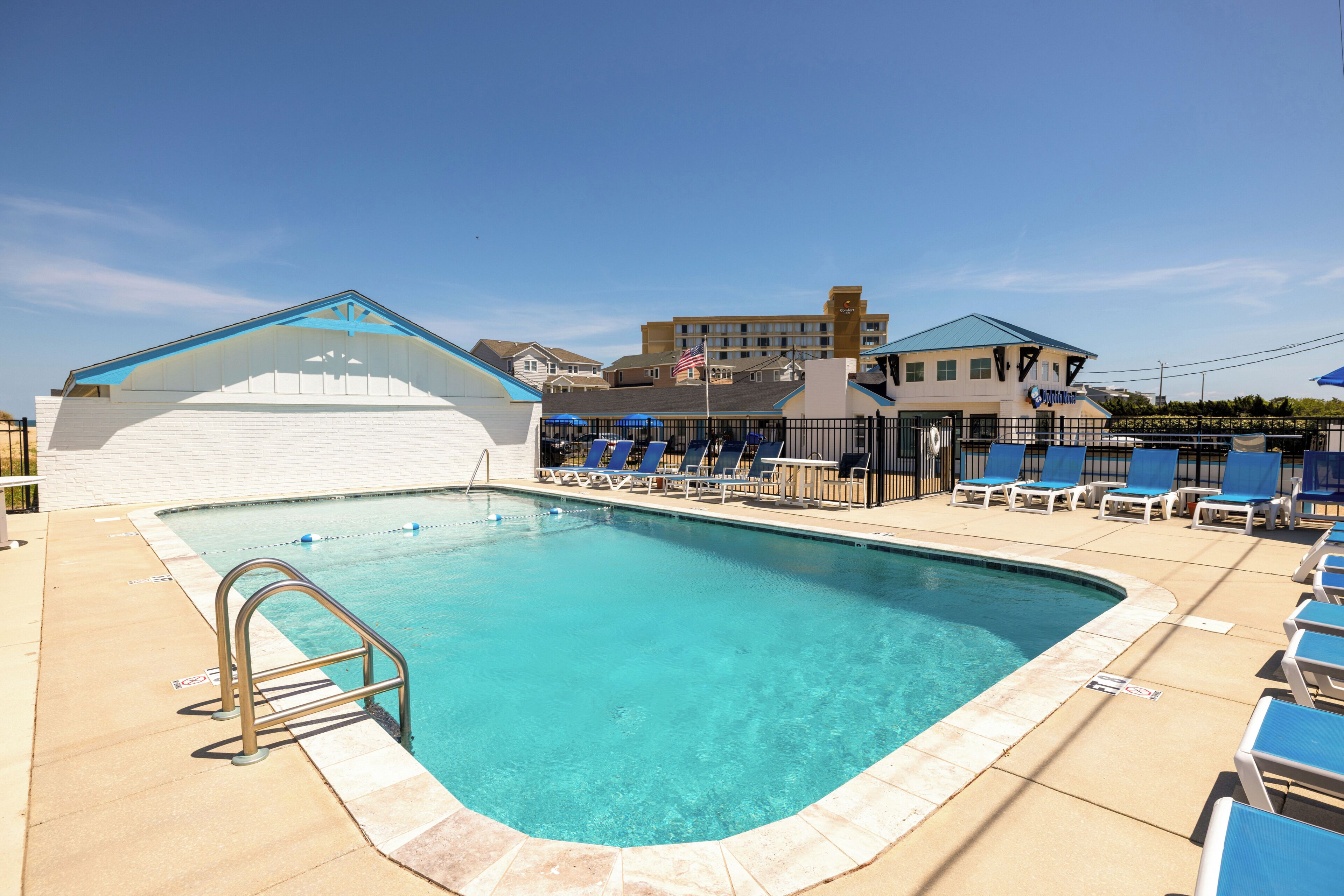 Une piscine avec des chaises longues, un poste de surveillance pour les sauveteurs et un bâtiment avec un toit bleu en arrière-plan.