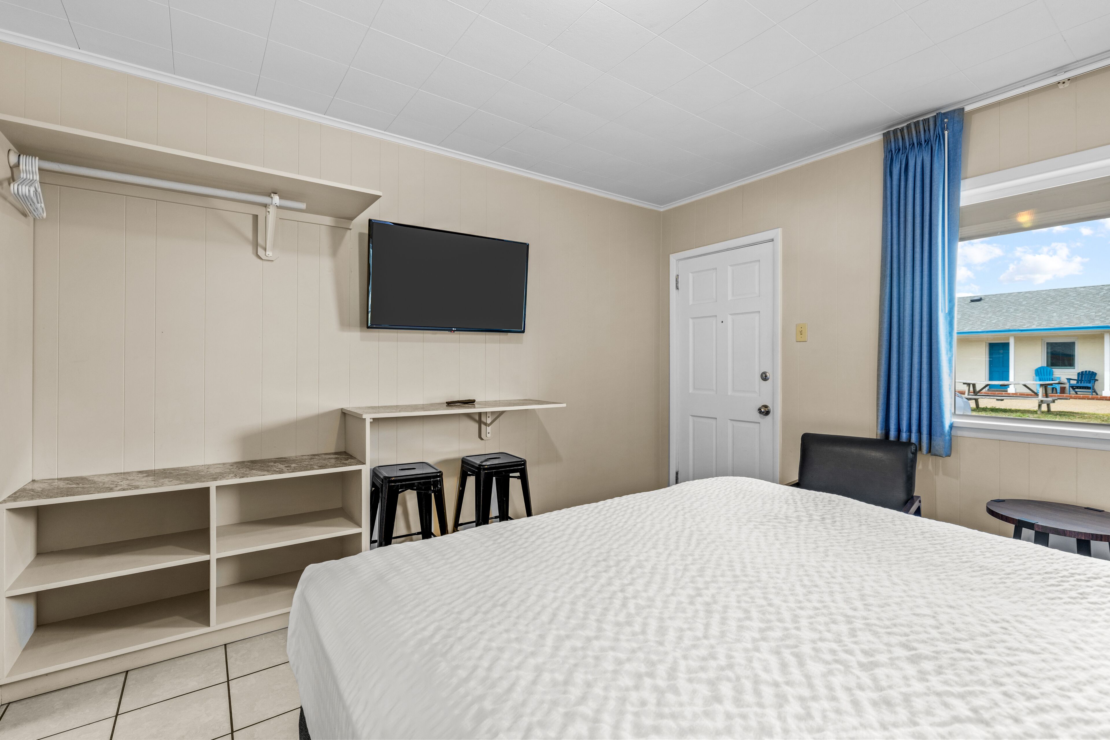 A hotel room with a bed, a TV mounted on the wall, a coat rack, and a window with curtains.