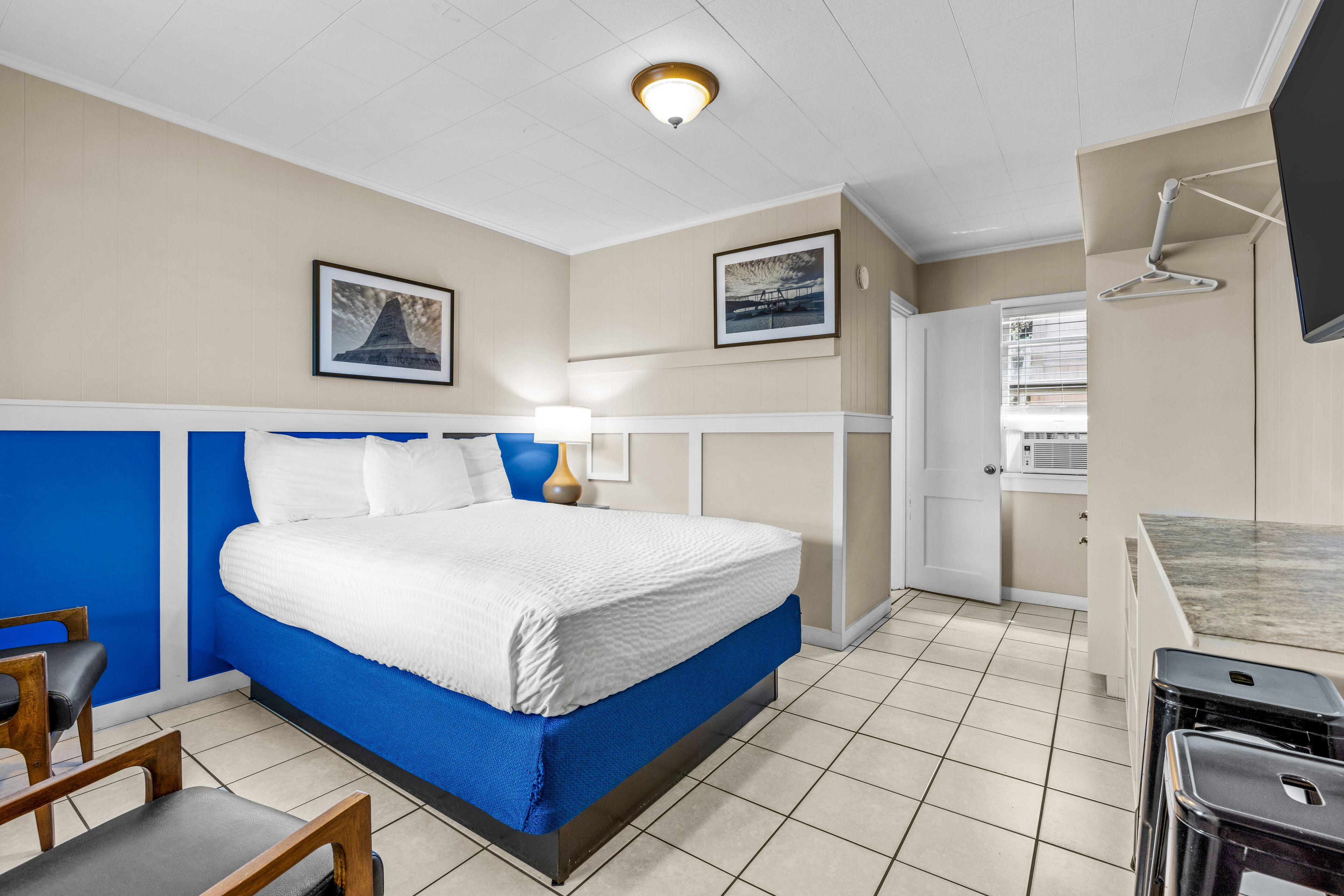 Una habitación de hotel con cama, escritorio, silla, lámpara y televisor.