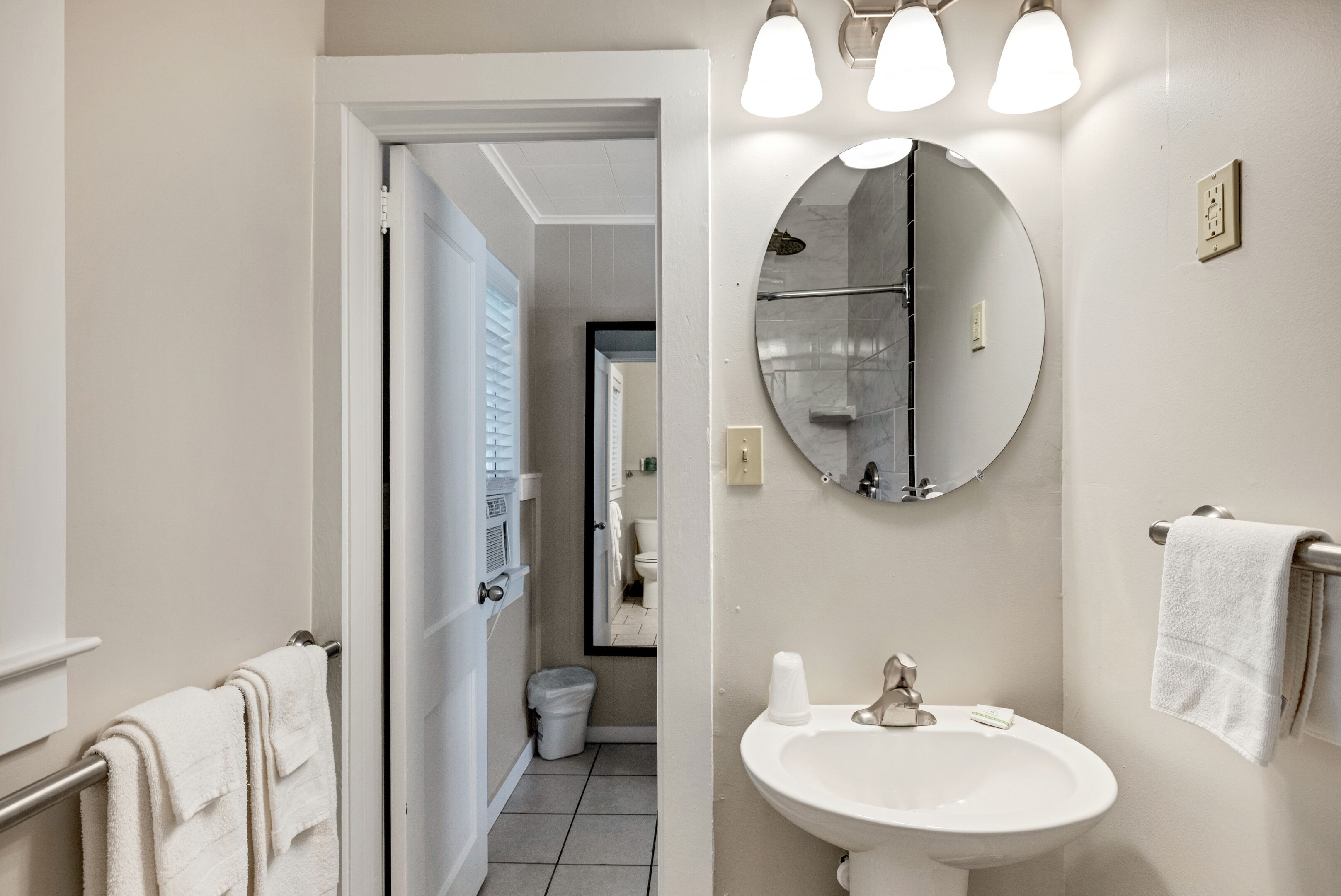 A modern bathroom with a white sink, a round mirror, and a towel rack.