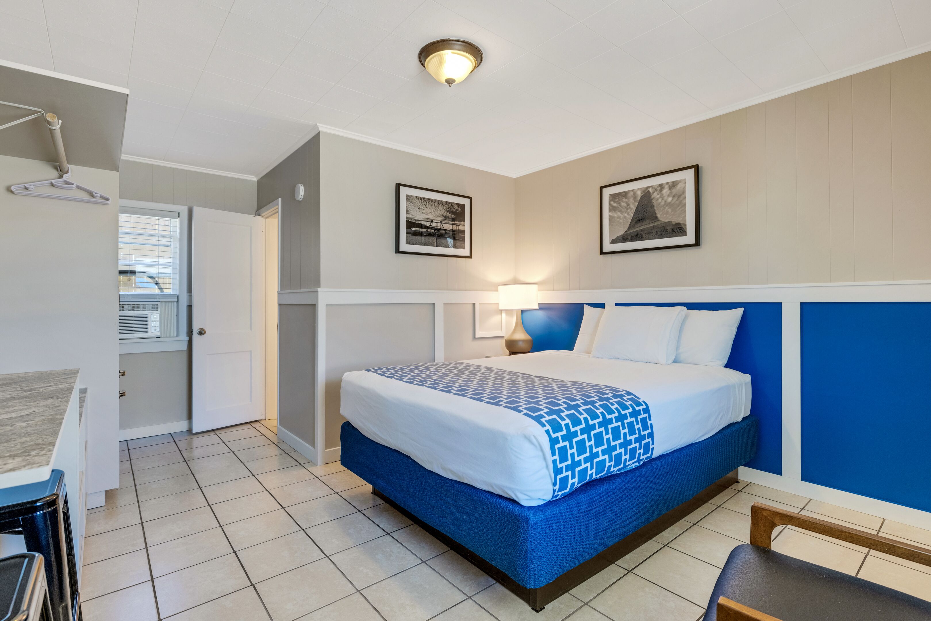 Una camera d'albergo con un letto, una scrivania e una sedia. Due quadri appesi alla parete.