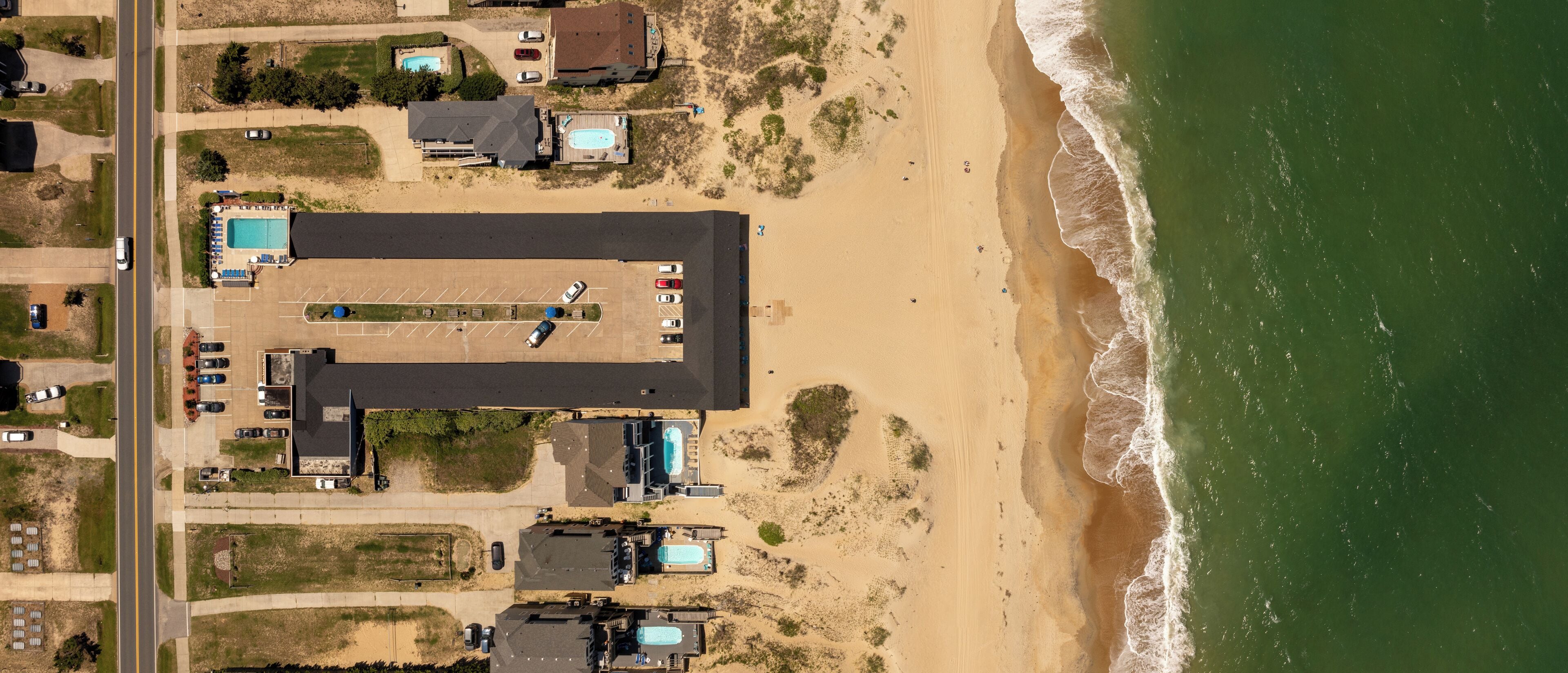 Vista aérea de uma propriedade costeira com várias piscinas, amplo espaço de estacionamento e acesso direto à praia.