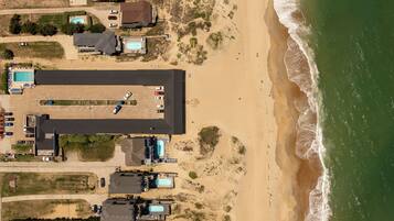 Vista aérea de uma propriedade costeira com várias piscinas, amplo espaço de estacionamento e acesso direto à praia.