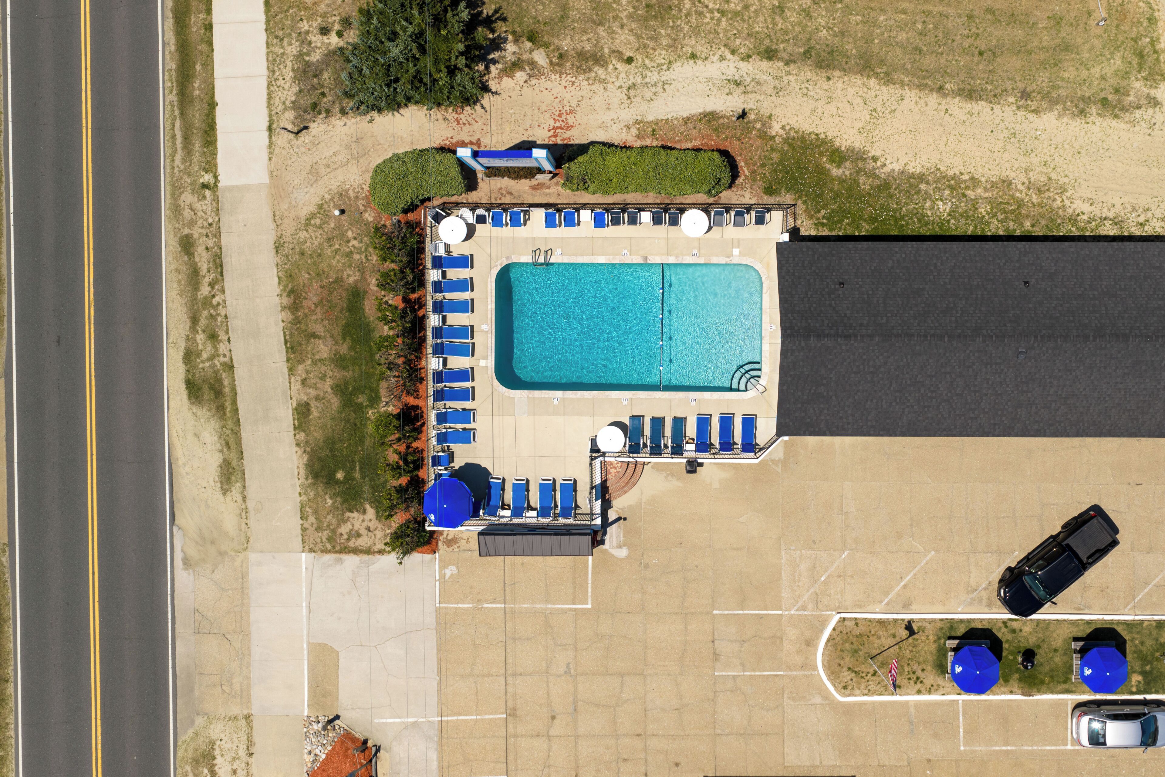 An aerial view of a hotel with a swimming pool, lounge chairs, and a parking lot.