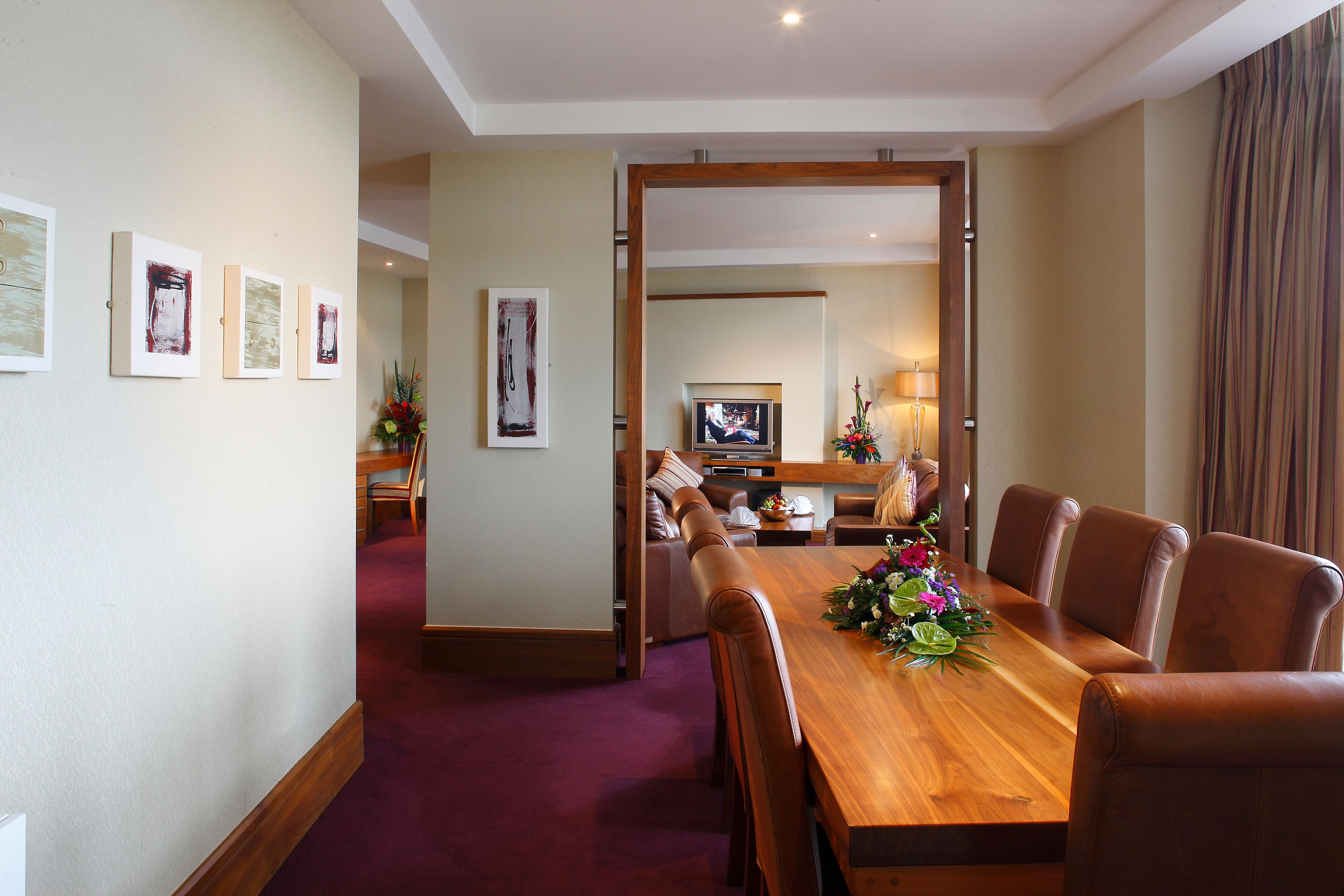 A hotel dining area with a wooden table, leather chairs, and framed artwork on the walls.