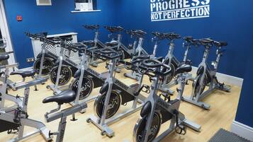 A gym with multiple spinning bikes arranged in rows, a motivational quote on the wall, and a small window.