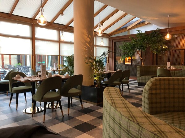 A restaurant with checkered flooring, green upholstered chairs, and hanging pendant lights.
