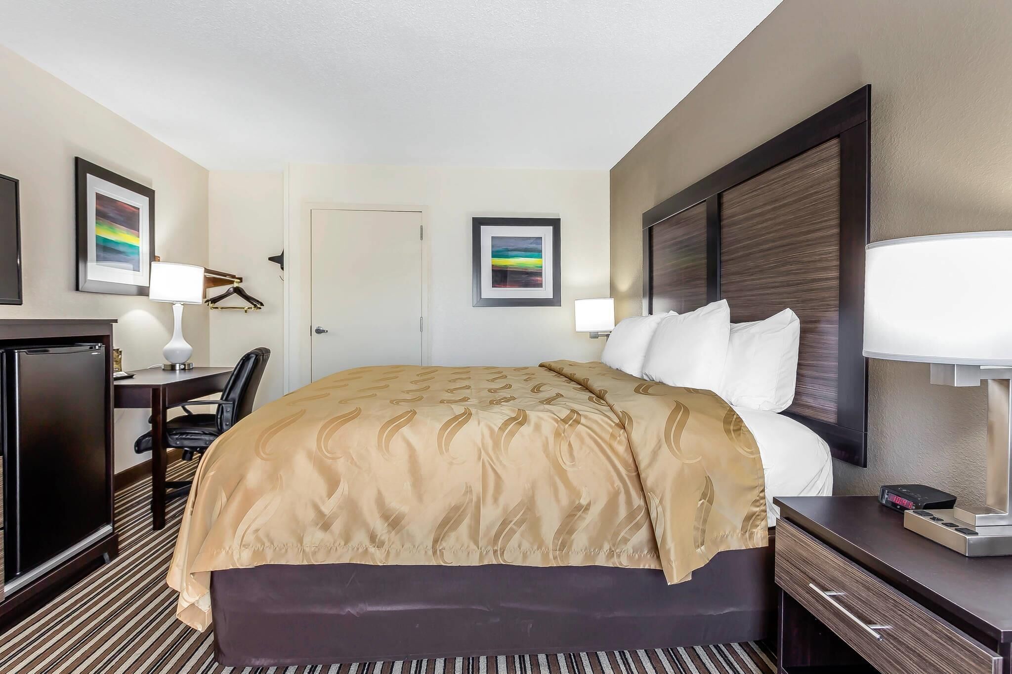A hotel room with a bed, bedside table, lamp, desk, chair, and a television.