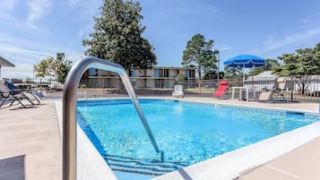 A swimming pool with a metal ladder, lounge chairs, and a blue umbrella.