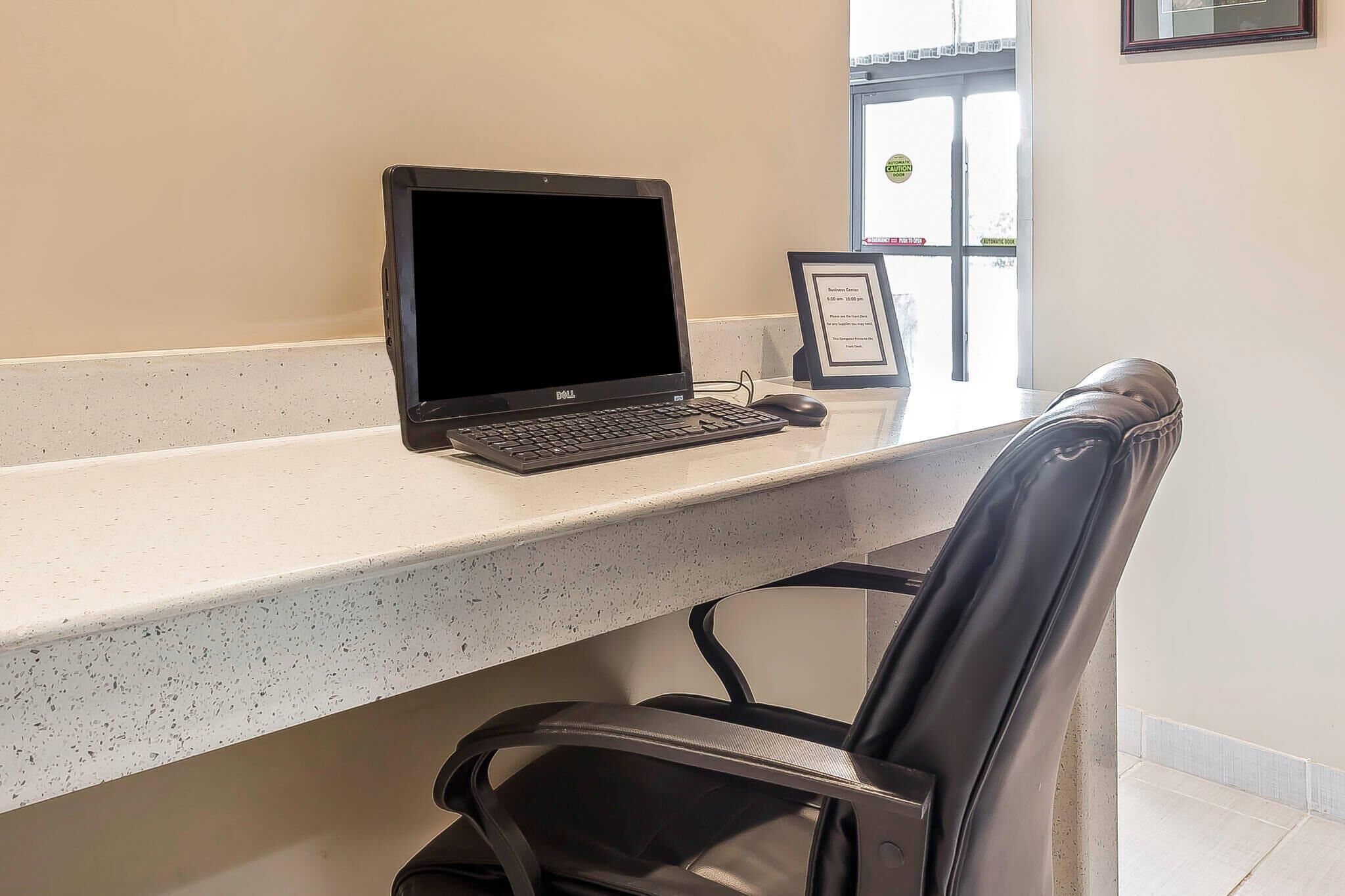 A desk with a laptop, a framed certificate, and a chair in a room with a window.