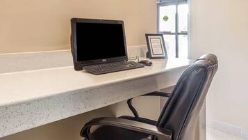 A desk with a laptop, a framed certificate, and a chair in a room with a window.
