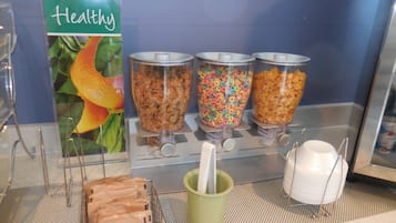 En frukostbuffé med olika sorters flingor, en skylt med texten ”Hälsosamt” och en grön mugghållare.