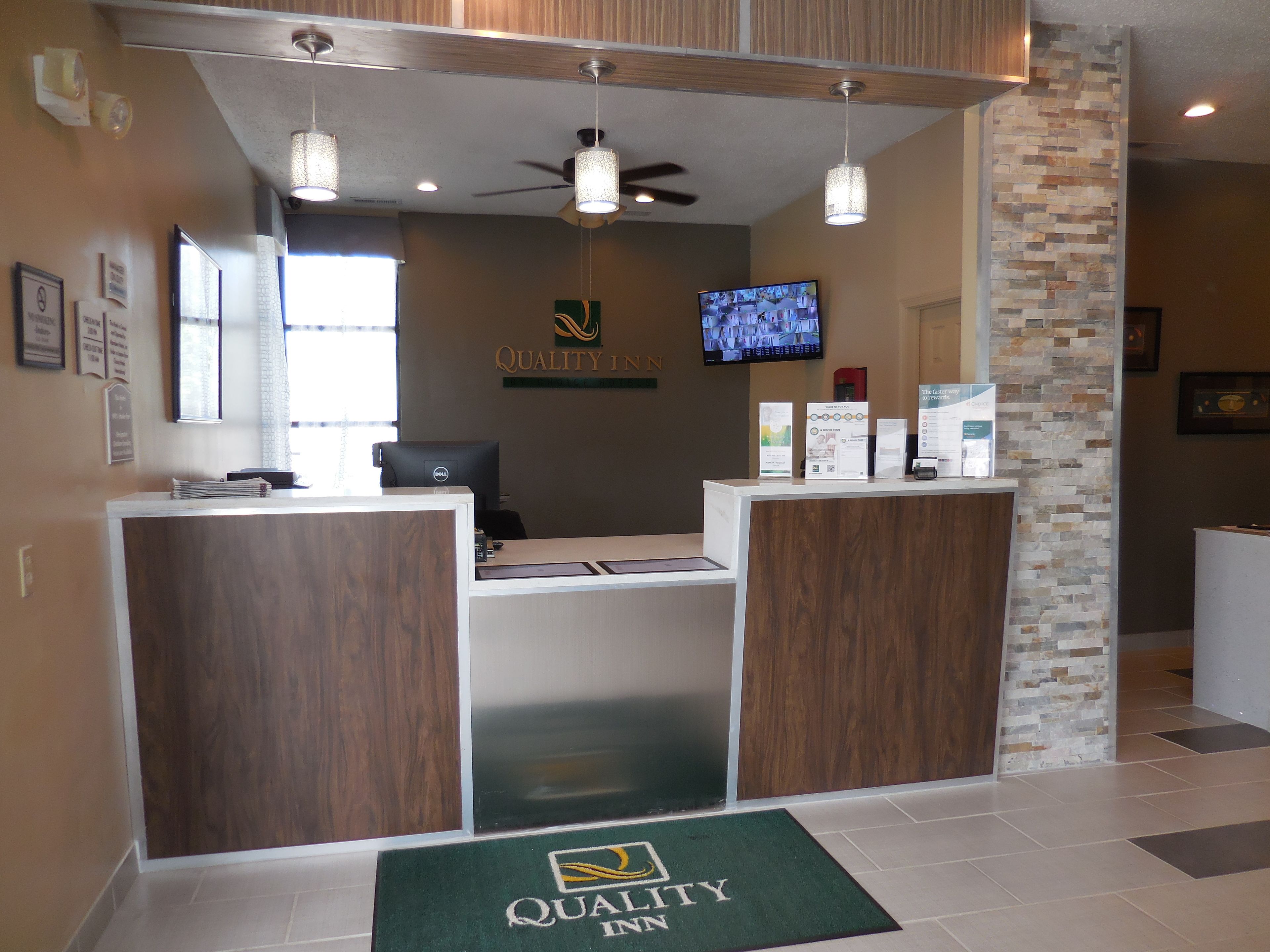 A reception area with a desk, a computer, a television, and a wall-mounted sign that reads "QUALITY INN".