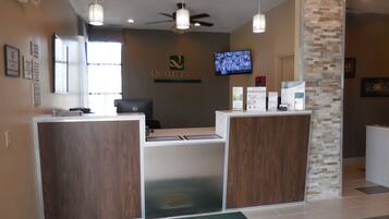 A reception area with a desk, a computer, a television, and a wall-mounted sign that reads "QUALITY INN".