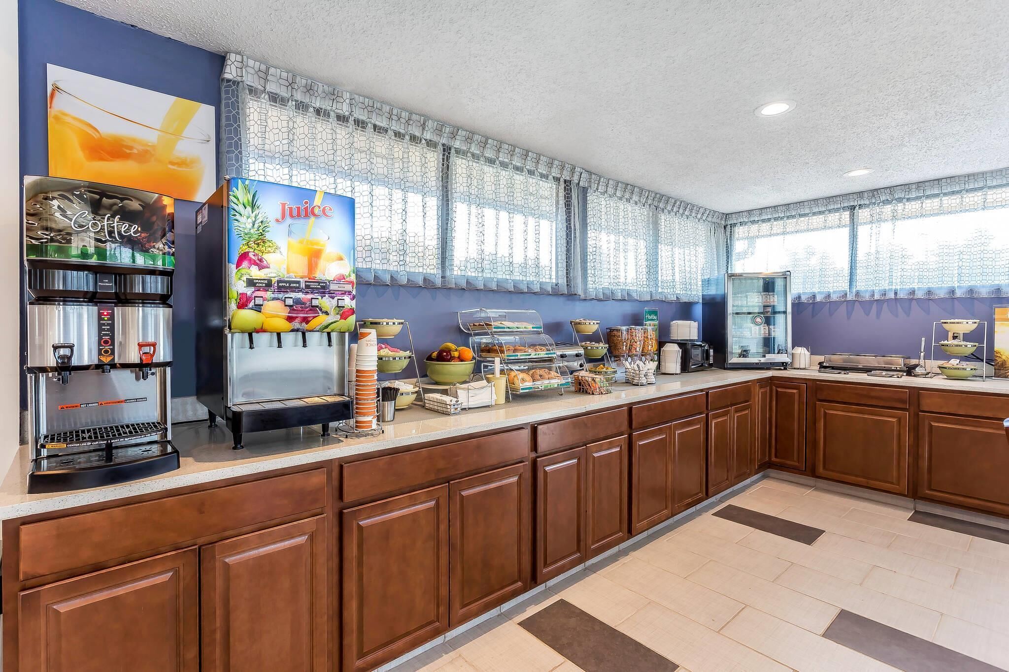 A breakfast bar with coffee and juice dispensers, a fruit display, and a bread station.