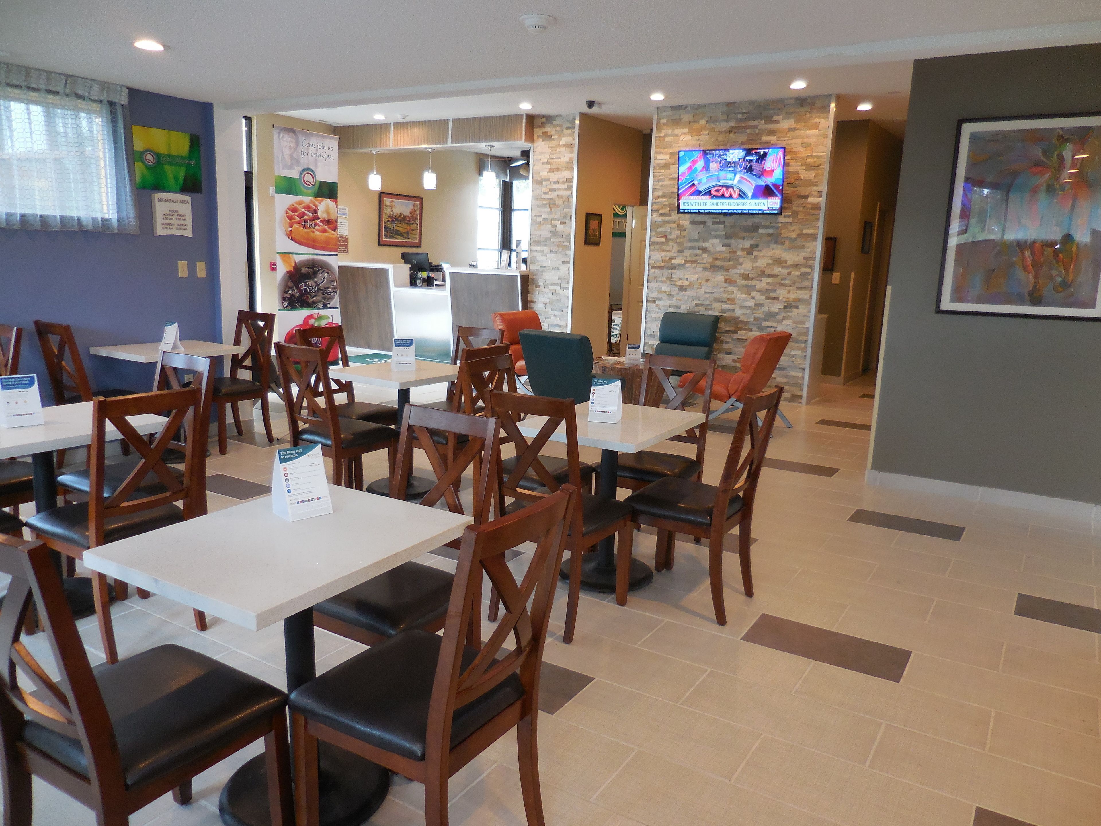 A restaurant with multiple tables and chairs, a kitchen area, and a TV screen displaying a program.