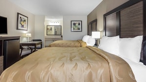 A hotel room with a large bed, a desk, a chair, a TV, and artwork on the walls. - Quality Inn Pinehurst Area (Aberdeen)