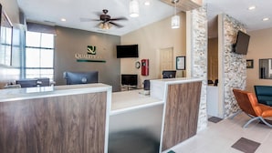 A reception area with a wooden reception desk, a flat-screen TV, a clock, and a coffee machine. - Quality Inn Pinehurst Area (Aberdeen)