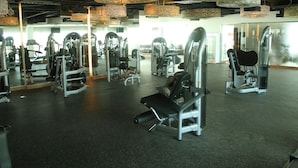 Une salle de sport équipée de divers appareils d’exercice, dotée de murs recouverts de miroirs et ornée de motifs décoratifs au plafond.
