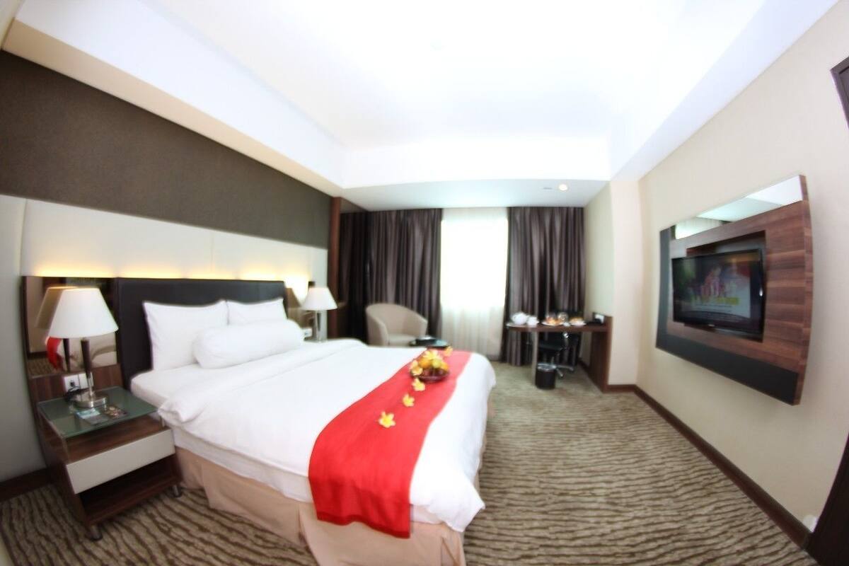 Une chambre d’hôtel avec un grand lit, un bureau, une chaise, un téléviseur fixé au mur et un sol recouvert de moquette.