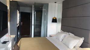 A modern hotel room with a large bed, a bedside table, a TV, and a glass shower enclosure. - Apollonia Royale Hotel (Angeles City)
