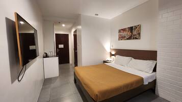 A hotel room with a bed, a flat-screen TV, a desk, and a door leading to a hallway.