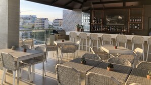 An outdoor bar area with wicker furniture and a grill, overlooking a cityscape. - Apollonia Royale Hotel (Angeles City)