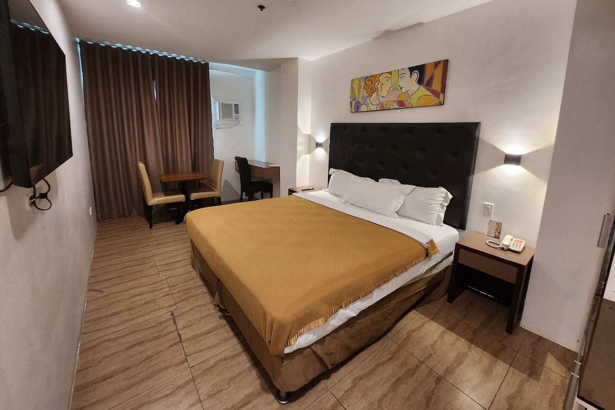 A hotel room with a large bed, a desk, a chair, a TV, and a painting on the wall.