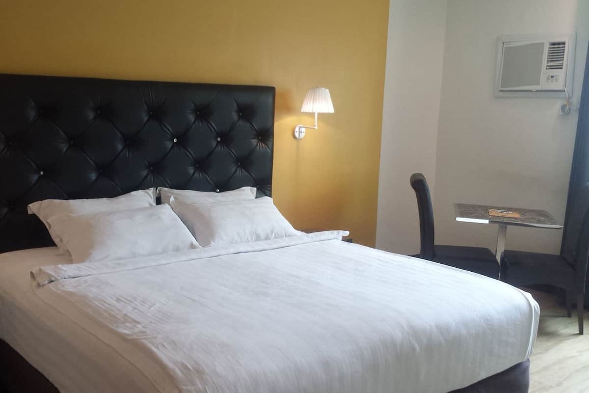 A hotel room with a large bed, two bedside lamps, a small table, and an air conditioning unit on the wall.