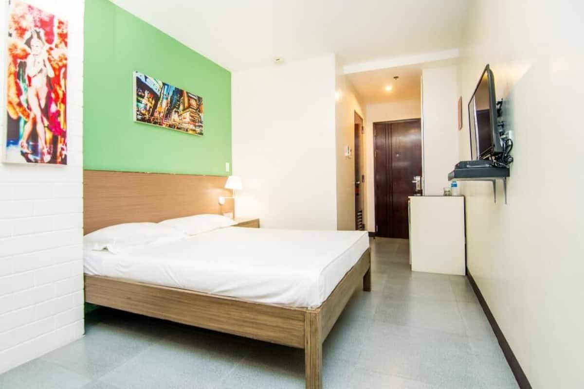 A hotel room with a bed, a nightstand, a desk, a mirror, and a green wall with a picture.