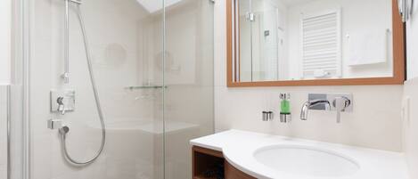 A modern bathroom with a glass-enclosed shower, a wooden vanity with a white sink, and a large mirror.