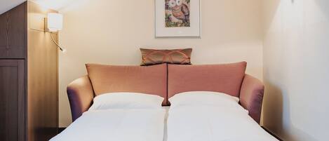 A neatly made bed in a room with a sloped ceiling, a framed picture on the wall, and a lamp on the side.