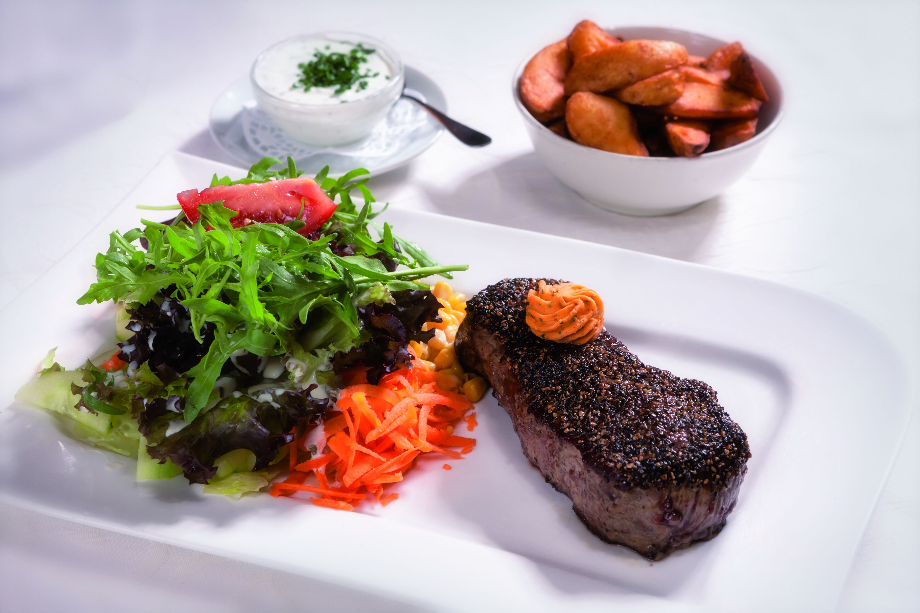 Une assiette avec un steak, une salade et des pommes de terre rôties.