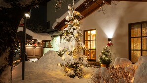 Un paisaje nevado con un árbol de Navidad decorado frente a un edificio de grandes ventanales y fachada de madera.