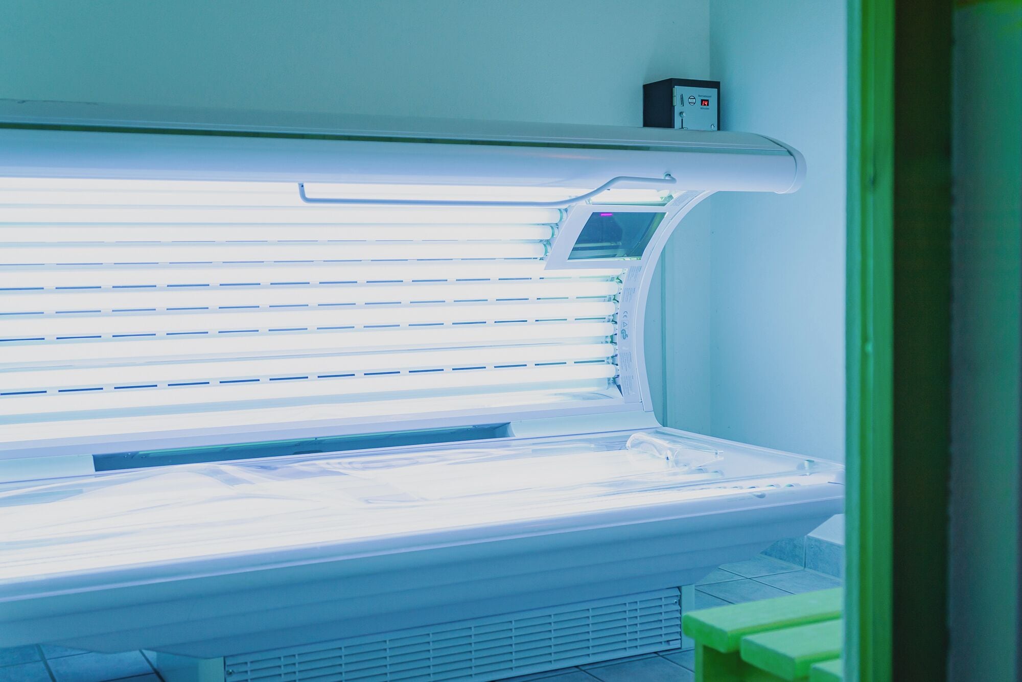 Una cama bronceadora con un panel de control y un banco verde.