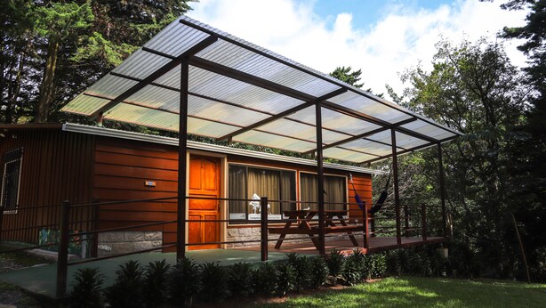 Een modern huis met een grote glazen uitbouw, een houten gevel en een overdekt terras.